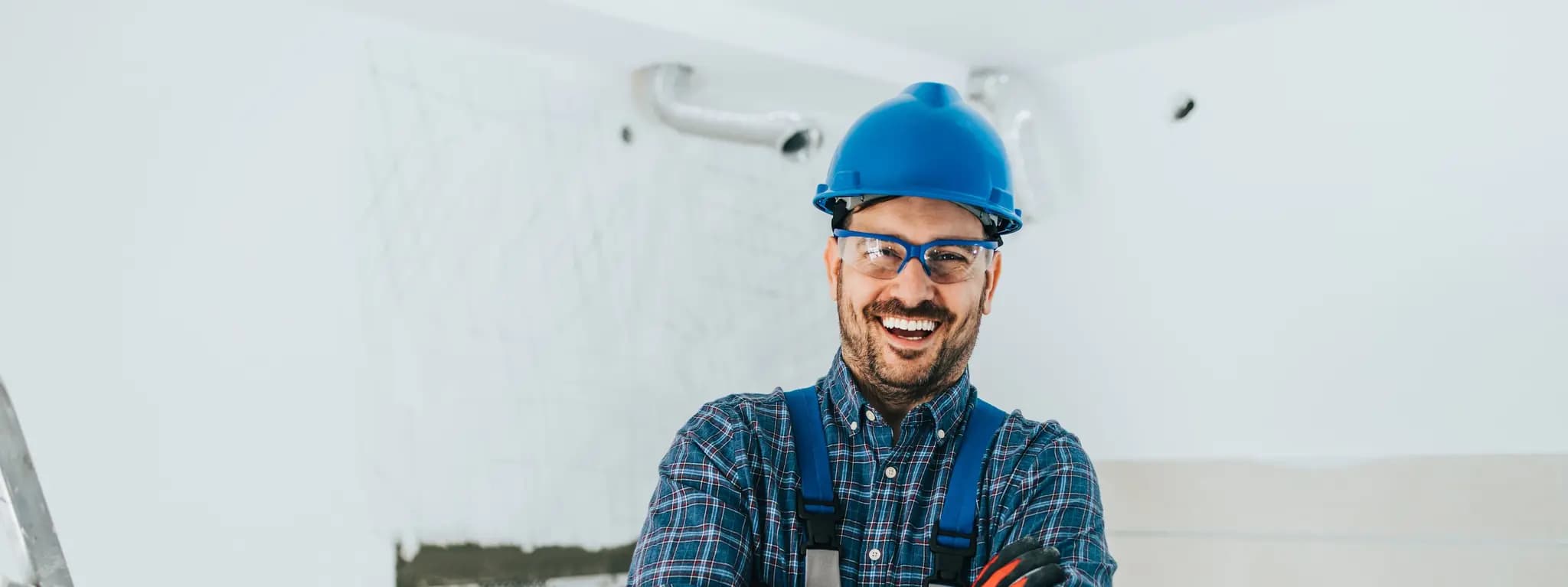 A middle aged man with a blue hardhat crossing his arms while standing and smiling.